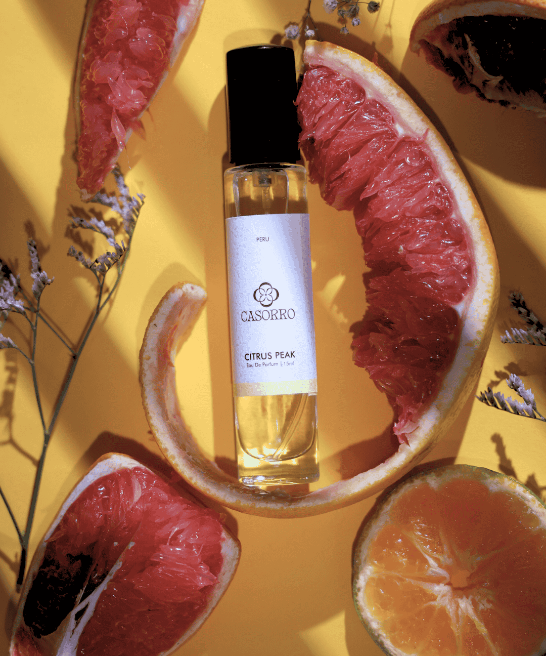 Casorro citrus peel perfume bottle surrounded by sliced grapefruits on a yellow background