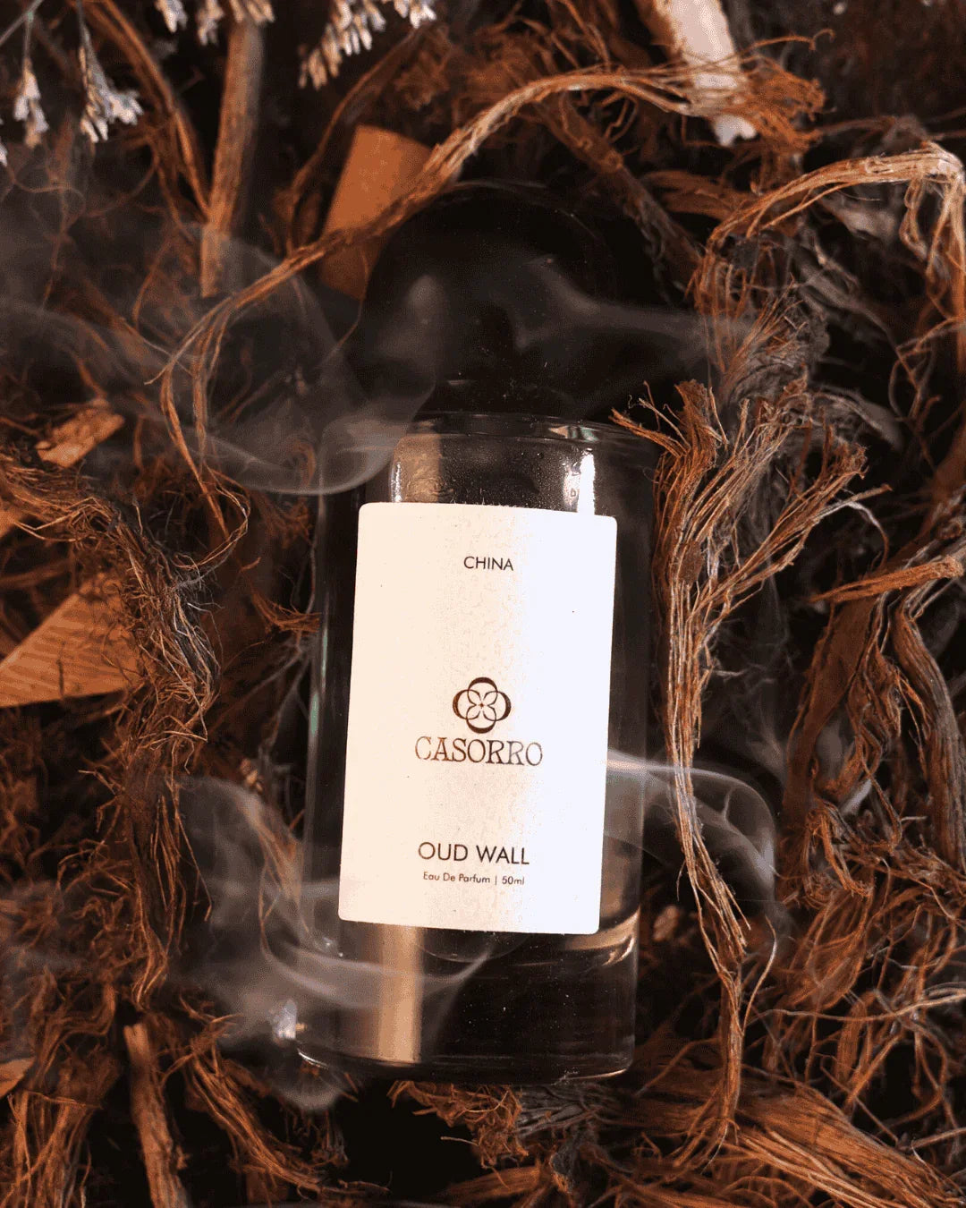 Oud Wall perfume bottle with black cap on rustic wooden background and swirling smoke