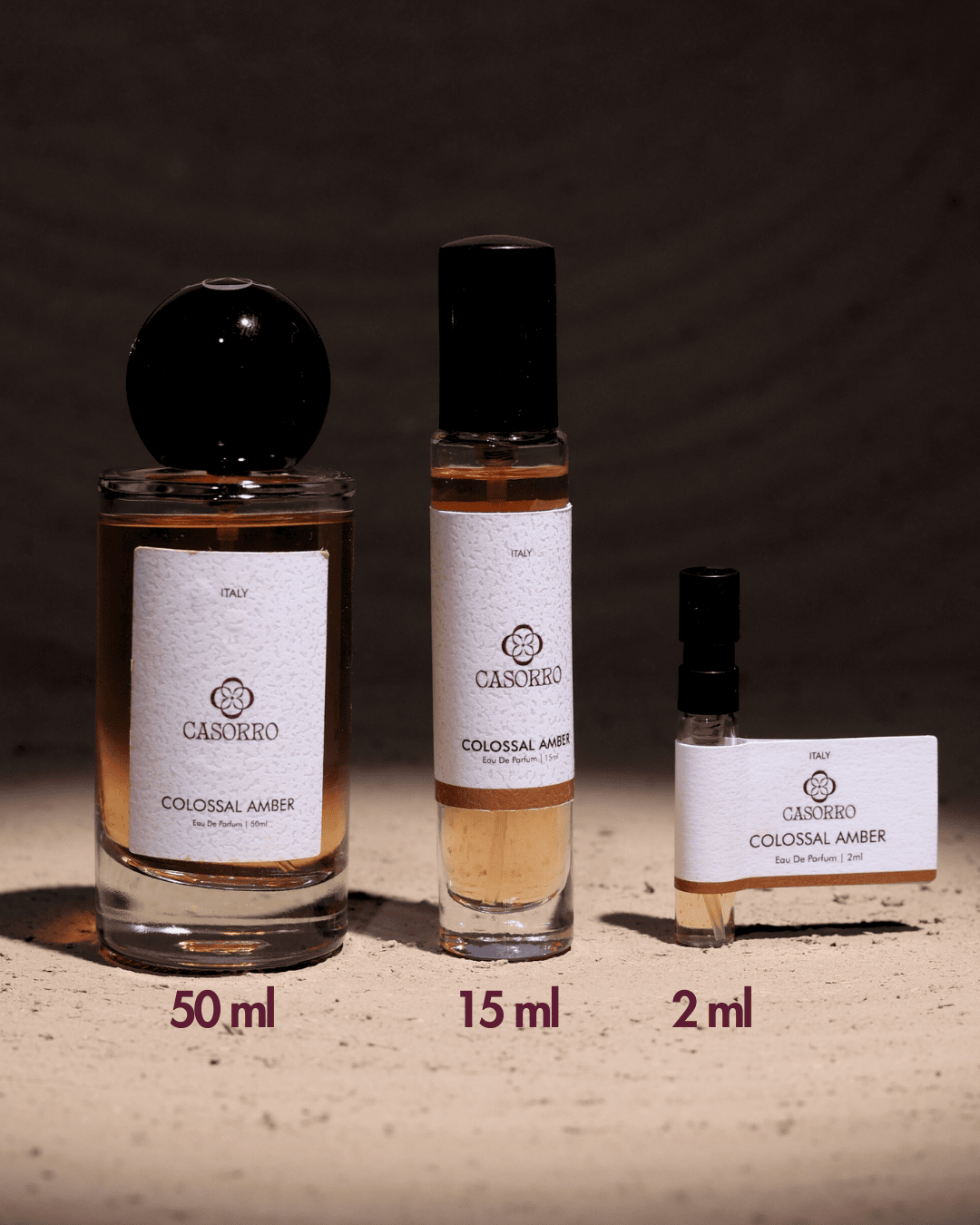 Three Casorro Colossal Amber perfume bottles of different sizes on a dark background