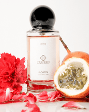 Perfume bottle labeled 'Casorro' with red flowers and a halved passion fruit on a white background