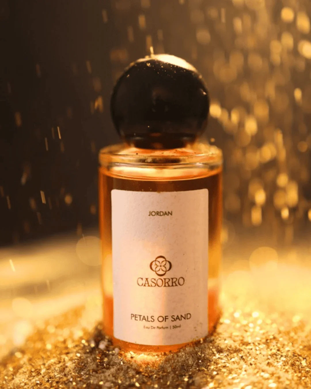 Luxury perfume bottle labeled 'Petals of Sand' on golden sand with sparkling light effects