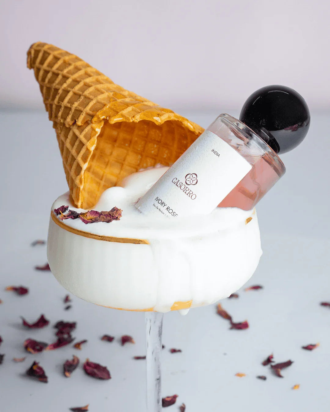 Ivory Rose perfume bottle with pink liquid, waffle cone, foam, and rose petals in a glass.