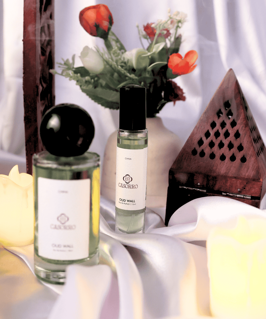 Two perfume bottles on a white surface with flowers in the background