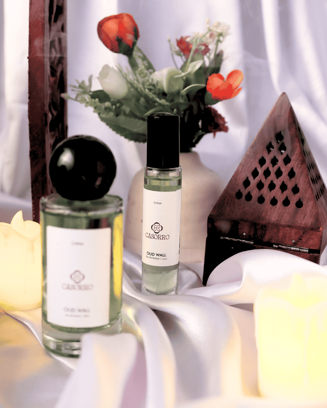 Two perfume bottles on a white surface with flowers in the background